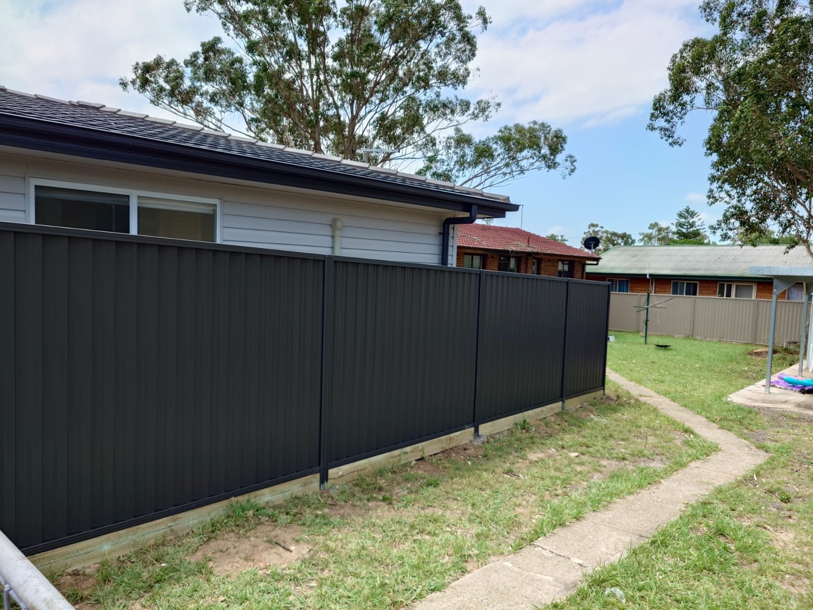 Charcoal Colorbond fence along a backyard lawn with a garden path