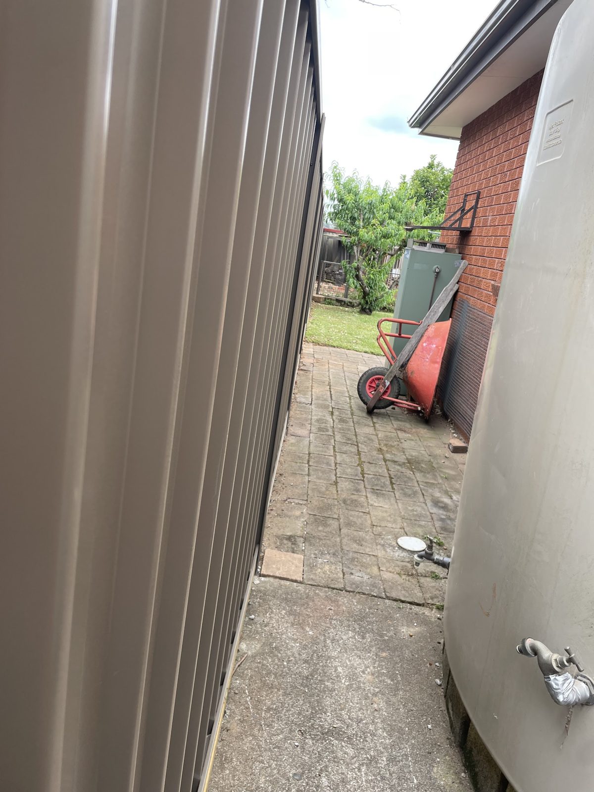 Cream Colorbond panels running down a narrow side passage beside a brick house