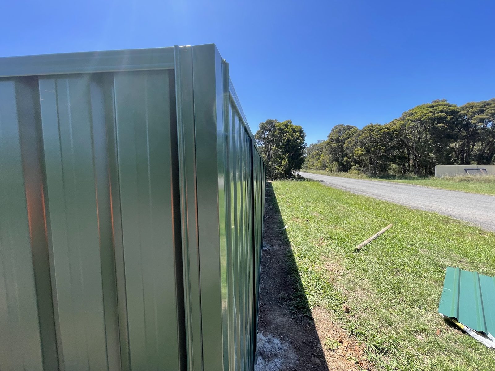 Close view of a green Colorbond fence corner beside a grassy roadside verge